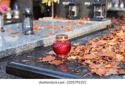 All Saints Day. Candles on graves. Autumn and leaves between candles on the graves of the dead in the cemetery. - Shutterstock ID 2335791551