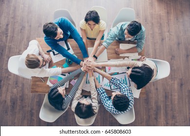 All together! Topview of businesspeople putting their hands on top of each other in nice light workstation, wearing casual clothes. Conception of successful teambuilding