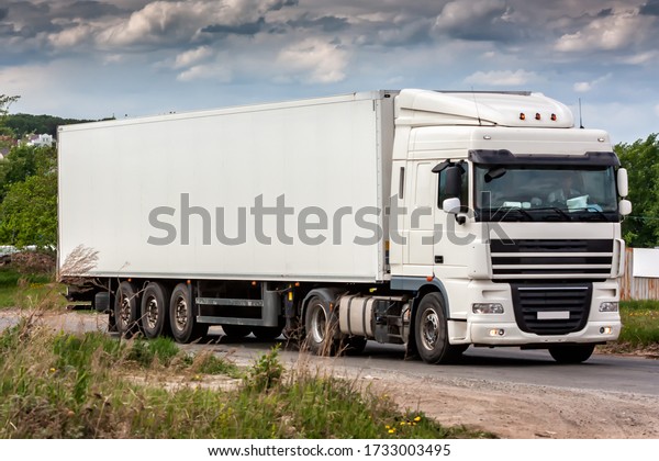 All white long-distance truck with a\
semitrailer moves in the\
countryside