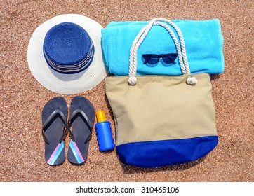 All You Need For A Summer Vacation At The Beach With A Sunhat, Flip Flops, Towel, Sunglasses, Sunscreen And Beach Bag Neatly Laid Out On A Sandy Tropical Beach, Overhead View