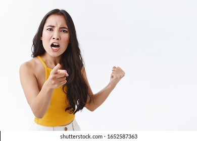 Its all your fault. Angry and upset outraged east-asian woman blame someone and complaining, frowning making furious grimace as pointing finger at camera, make accusations and fighting