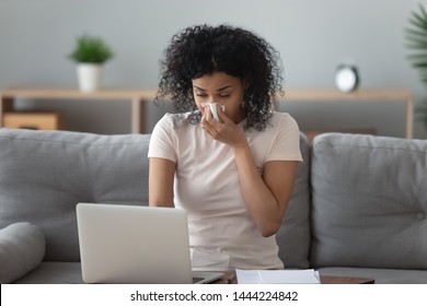 Allergic African Woman Blowing Nose In Tissue Sit On Sofa At Home Office Study Work On Laptop, Ill Sick Black Girl Got Flu Caught Cold Sneeze In Tissue Having Allergy Symptoms Coughing Holding Napkin