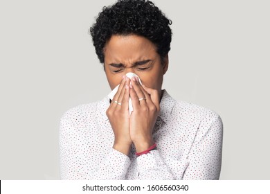 Allergic ill young african woman holding tissue blowing running nose got chill sneezing in handkerchief feels unwell, head shot portrait isolated on grey background, influenza virus snuffles concept - Powered by Shutterstock