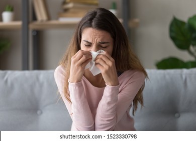 Allergic ill young woman sit on sofa holding tissue blowing running nose got fever caught cold sneezing in handkerchief, sick girl having influenza virus flu symptom coughing at home, allergy concept - Shutterstock ID 1523330798