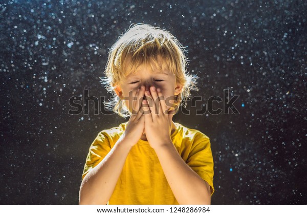 Allergy to dust. Boy sneezes\
because he is allergic to dust. Dust flies in the air backlit by\
light