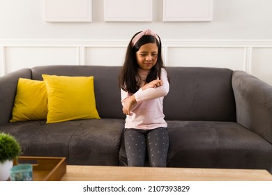 Allergy Reaction. Beautiful Elementary Kid With An Itchy Skin Scratching Her Arms While Sitting On The Sofa