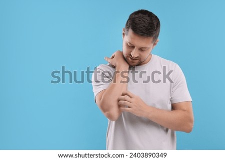 Allergy symptom. Man scratching his arm on light blue background. Space for text