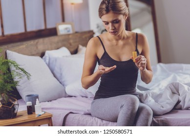 Alleviating pain. Beautiful young woman sitting on the bed and taking painkillers while wanting to alleviate some pain - Shutterstock ID 1250580571
