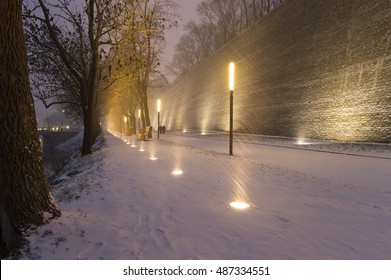 Alley With Lights, Snowfall And Stone Wall On The Right