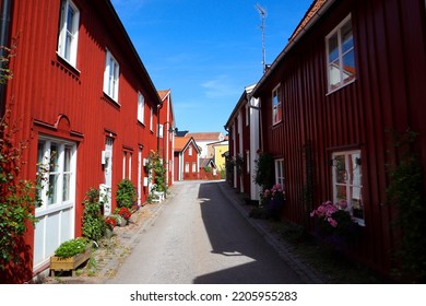 An Alley Way On Västervik, Sweden With Red Traditional Swedish Houses With Shade On The Right Side In Västervik, Sweden On A Blue Sky Summer Day