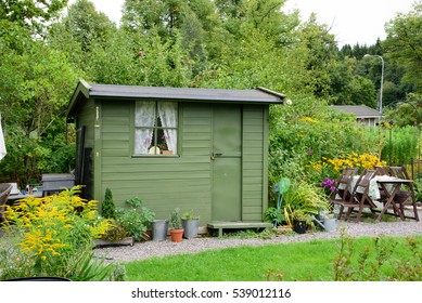 Allotment Garden. A Green Wooden Shed With Green Door And Window. Table And Chairs.