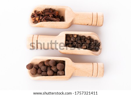 allspice, black pepper and cloves in wooden spoons isolated on a white background