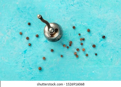 Allspice, Jamaica Pepper. Black Peppercorns With A Vintage Pepper Mill, Overhead Shot On A Teal Blue Background With A Place For Text