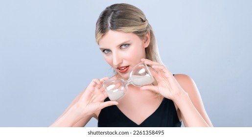 Alluring beauty model holding hourglass in forever young beauty concept of anti-aging skincare treatment for woman. Beautiful caucasian women portrait with perfect makeup in isolated background.