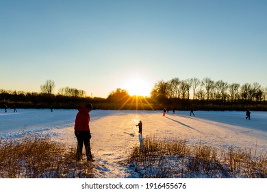 Almere, Flevoland, Holland - February 12 2021 - Ice Skating People During Sunset On A Lake In Nature Park Oostvaardersplassen In Almere, The Nederlands