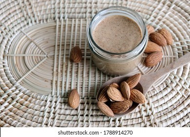 Almond Butter In Glass Jar And Almond Raw In Spoon On Wooden Background.