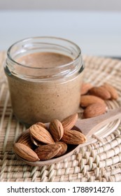 Almond Butter In Glass Jar And Almond Raw In Spoon On Wooden Background.