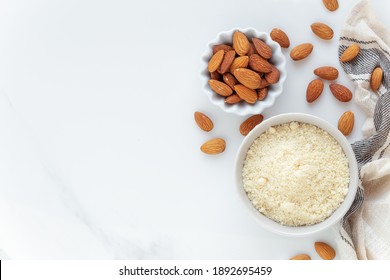 Almond flour and almonds in bowls as a Gluten free food concept. Overhead view with prenty of copyspace against white marble background