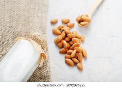 Almond milk in a bottle with a handful of grains and a wooden spoon with a burlap cloth on a light background. Top view - Powered by Shutterstock