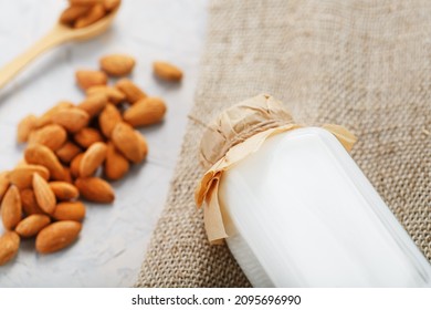 Almond milk in a bottle with a handful of grains and a wooden spoon with a burlap cloth on a light background. Top view - Powered by Shutterstock