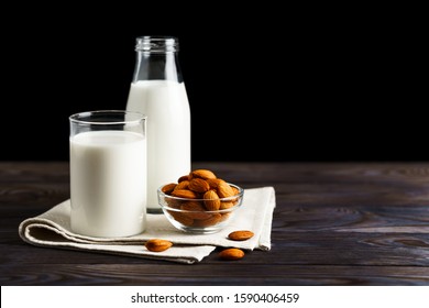 Almond milk in a glass mug and a refillable glass bottle, with almond nuts on a wooden table and black background.