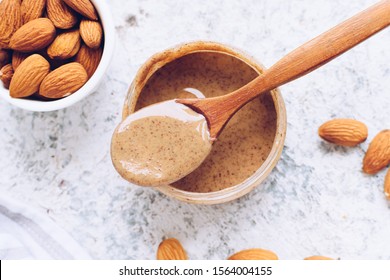 Almond nut butter in glass jar. Homemade raw organic almond nuts paste on grey background. Healthy natural food concept. Top view.