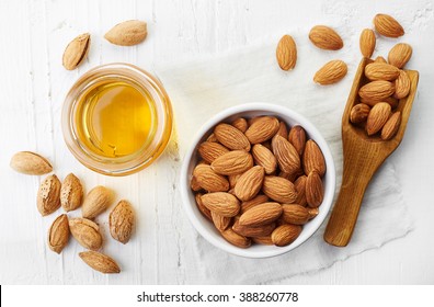 Almond oil and bowl of almonds on white wooden background. Top view