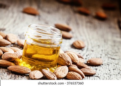 Almond oil in a small jar of almonds and nuts on an old wooden background, selective focus