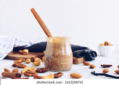 Almond, pecan and cashew nut butter in glass jar. Homemade raw organic mixed nuts paste with cinnamon and vanilla on white background. Healthy natural food concept. Copy space.