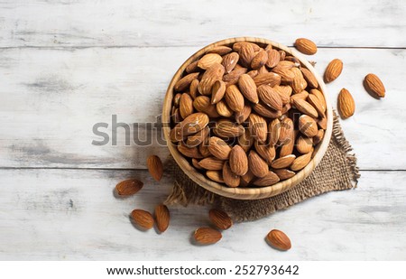 Almonds in brown bowl on wooden background