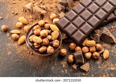 Almonds and hazelnuts with melted dark chocolate. Melted milk chocolate, cocoa powder, pieces and nuts on black background. Cooking handmade chocolate bars, desserts, sweets. Confectionery craft