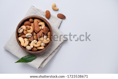 almonds, pistachios and cashews are placed in a wooden bowl on a linen napkin on a light grey background. Top view and copy space. Horizontal orientation