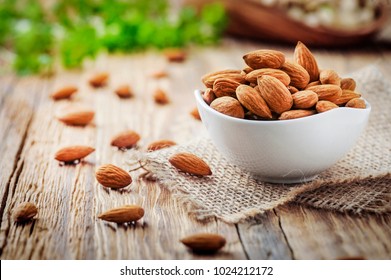 Almonds in white porcelain bowl on wooden table. Almond concept with copyspace.