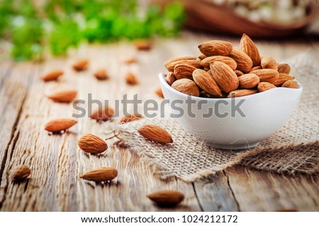 Almonds in white porcelain bowl on wooden table. Almond concept with copyspace.
