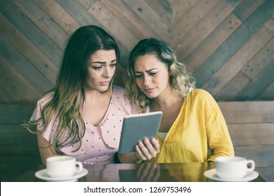 Almost Crying Young Women Reading Bad News Online. Sad Girls Watching Video Of Terrible Accident On Tablet Computer.  Shocking Information Concept