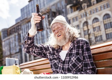 Almost empty. Cheerless drunk man looking at the bottle while drinking alcohol on the bench