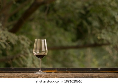 An Almost Empty Glass Of Red Wine Put On A Wooden Window Sill