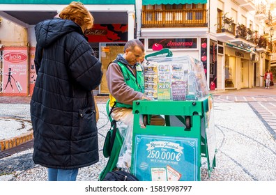 Almunecar, Granada/Spain November 11 2019
Lottery Customer Buying Lottery Tickets By A Street Vendor. The Vendors Are Easily Recognizable In Their Green Jackets. Lottery Is Very Popular In Spain