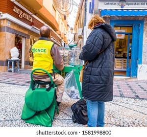 Almunecar, Granada/Spain November 11 2019
Lottery Customer Buying Lottery Tickets By A Street Vendor. The Vendors Are Easily Recognizable In Their Green Jackets. Lottery Is Very Popular In Spain