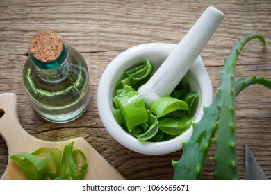 Aloe vera leaves, mortar full of chopped aloe, cutting board and bottle of aloe gel or infusion. Top view.