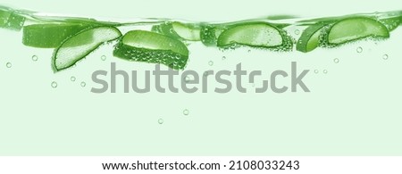 Aloe vera slices under water on green background. Copy space, banner.