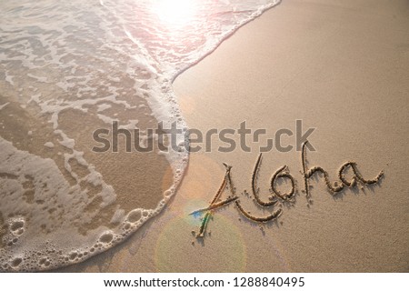 Aloha tropical vacation message handwritten on a smooth sand beach with incoming wave