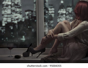 Alone beautiful woman sitting on window and looking on night city