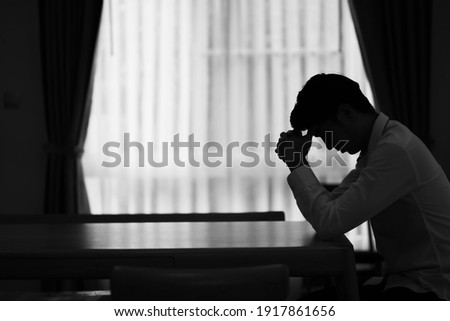 Alone Businessman silhouette sitting on the table closed with curtains in home, Depression and anxiety disorder concept.