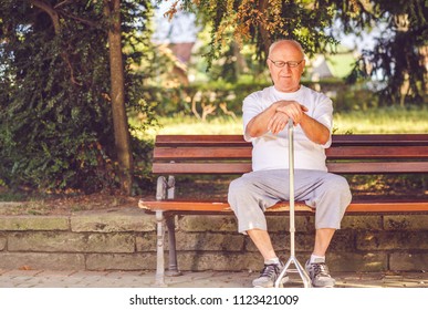 Alone Elderly Man With His Walking Stick Sitting On Bench In The Park
