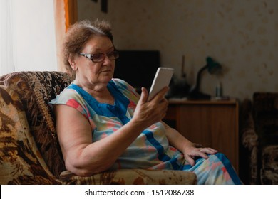 Alone elderly woman using mobile phone near the window in her living room. Internet in retirement - Powered by Shutterstock