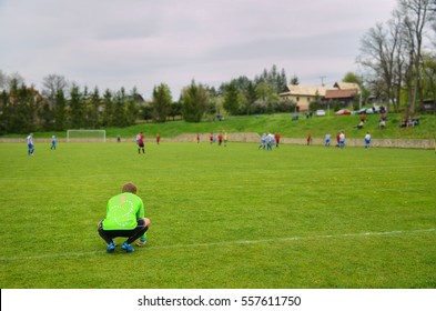 Alone Goalkeeper Standing On The Green Field And Looking At Team Mate Who Play Football In 