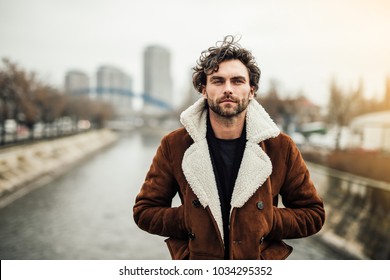 Alone Handsome Man With Beard And Winter Or Autumn Coat Standing Outside Next To A River And Thinking About Something Or Waiting For Someone