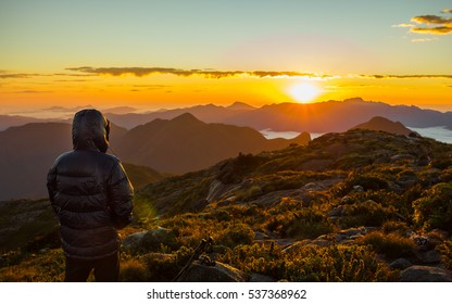 Alone Man With Down Jacket Watching The Sunrise At The Mountains