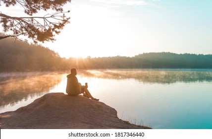 Alone Man Meditating And Relaxing On Beautiful Nature. Travel And Healthy Lifestyle Concept Lake And Mountains Sunny Landscape On Background Outdoor. Sustainable Climate Visuals